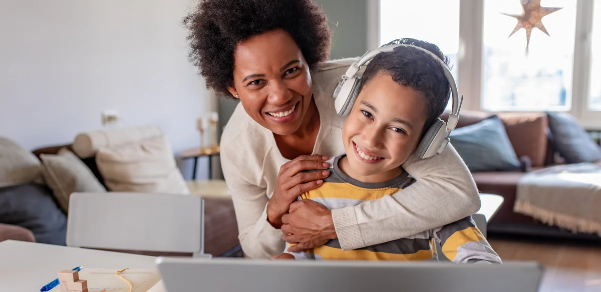 mother and son hugging and smiling at the camera while working on their laptop at home